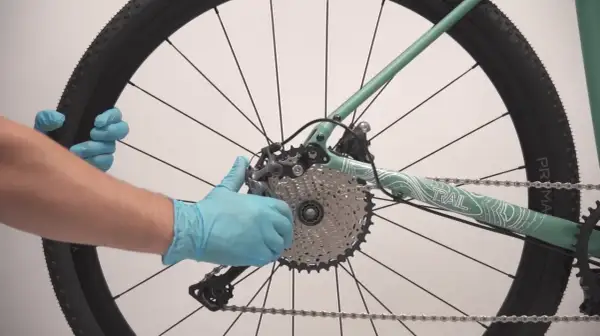 Maintenant, je vais démonter la roue arrière de ce vélo électrique. Les mains gantées tiennent la roue et le dérailleur.