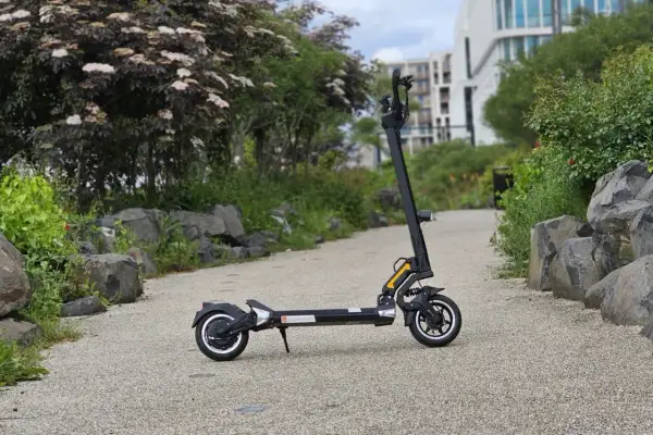 Trottinette électrique Dualtron Togo noire, sur un chemin pavé, avec des rochers et de la végétation.