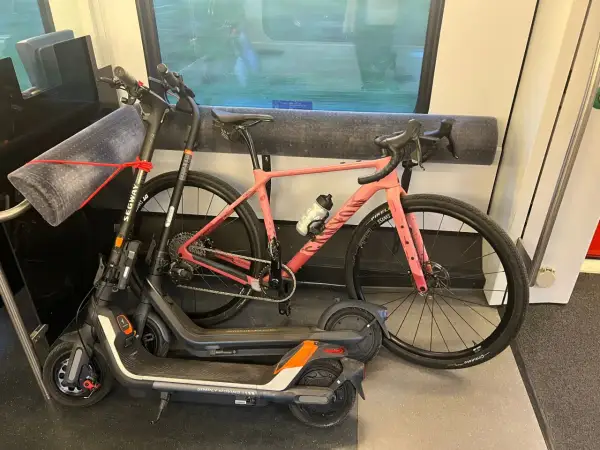 Une trottinette et un vélo rose sont rangés dans un compartiment de train, prêts pour l'aventure.