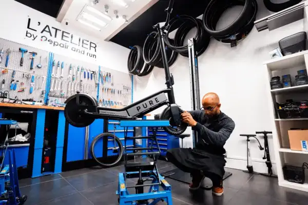 Un mécanicien ajuste une trottinette électrique PURE dans un atelier. Idéal pour ceux qui cherchent à vendre trottinette électrique ou à la faire réparer.