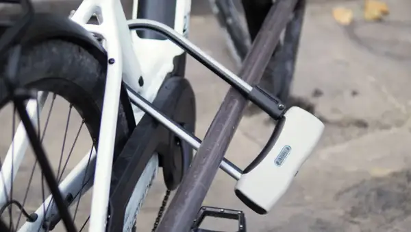 Un antivol pour vélo avec alarme intégrée protège un vélo blanc. Le cadenas en U est fixé au cadre et à la roue arrière.