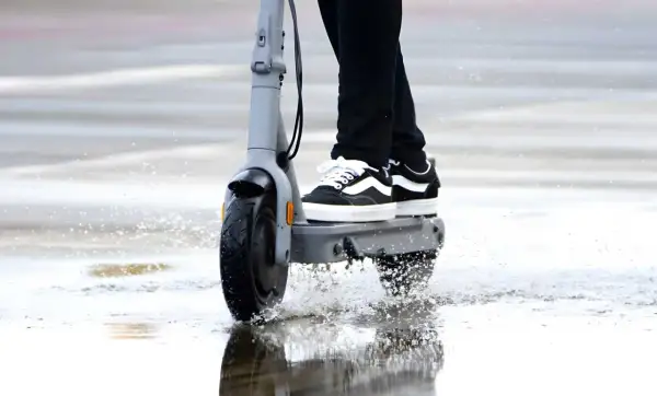 Trottinette électrique en action, éclaboussant l'eau sous la pluie. La protection ip54 assure une résistance à l'eau pour continuer le trajet.