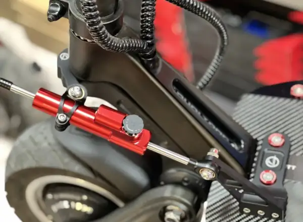 Amortisseur de direction trottinette rouge vif, fixé sur le châssis noir, prêt à améliorer la stabilité.