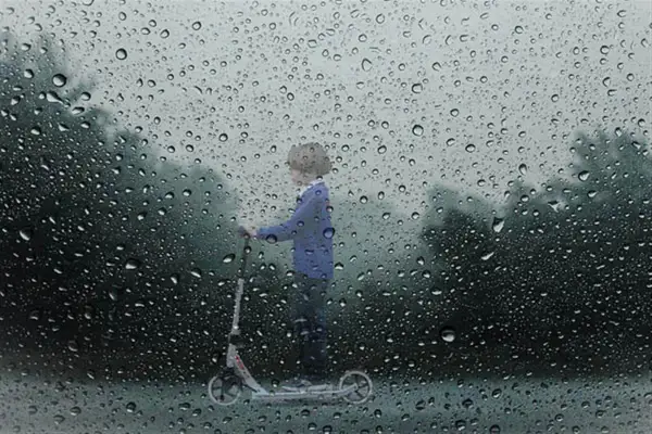 Un enfant sur une trottinette, sous la pluie. Le **signification IP54** protège de la poussière et des éclaboussures.