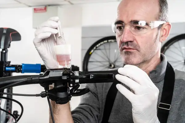 Un mécanicien effectue le purge frein a disque velo, ajoutant du liquide de frein avec une seringue.