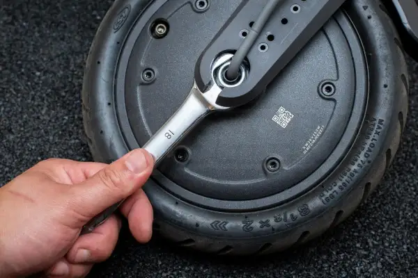 Main tenant utilise une clé pour changer la roue avant d'une trottinette électrique.