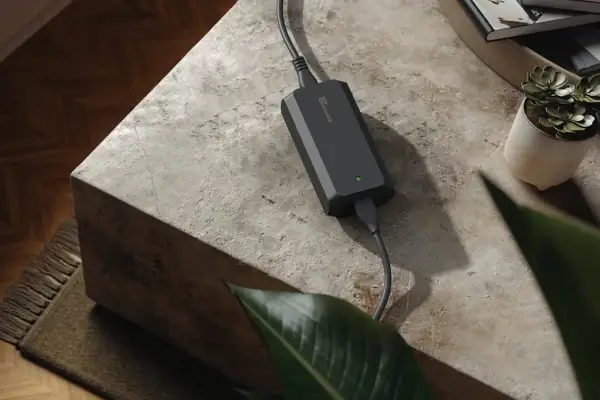 Chargeur 48v noir, compact et discret, posé sur une table en pierre. Une petite plante verte et des livres sont à proximité.