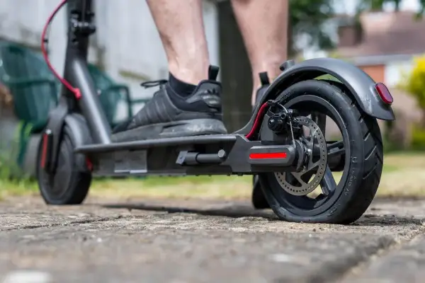 Pieds sur une trottinette électrique, le pneu arrière est visiblement crevé, rendant le trajet difficile.