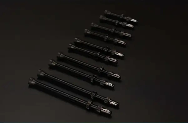 Plusieurs valves Schrader noires, alignées sur un fond sombre, prêtes pour une nouvelle aventure cycliste.