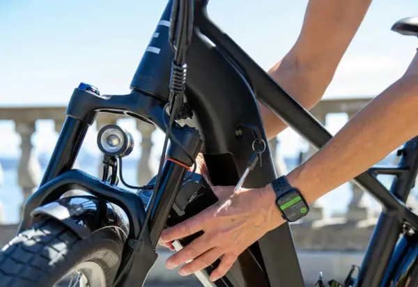 Main d'une personne âgée insérant la clé dans le cadre d'un vélo électrique. La montre connectée affiche "End Workout".