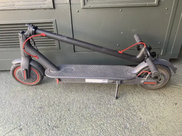 Trottinette électrique noire pliée, avec un câble rouge visible. Un kit d'étanchéité pour trottinette électrique pourrait être utile pour la protéger.