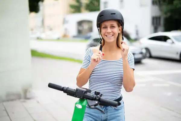 Jeune femme souriante ajustant son casque trottinette électrique, prête pour une balade en ville.
