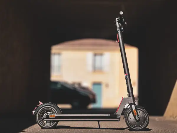 Trottinette électrique Wispeed T850 noire, vue de profil, devant une maison floue.
