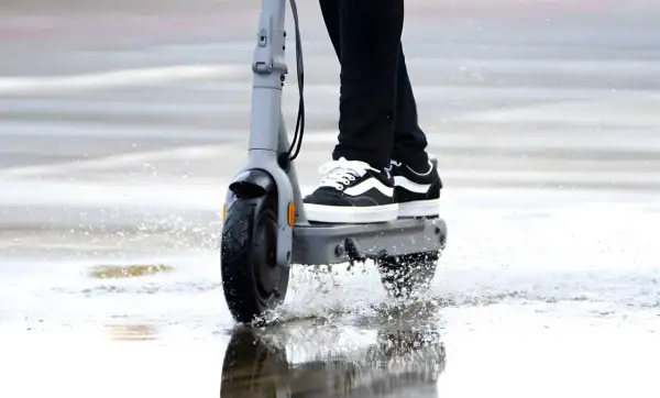 Une trottinette électrique roule dans une flaque d'eau, soulevant des éclaboussures. La question est : peut-on rouler sous la pluie avec une trottinette électrique ?