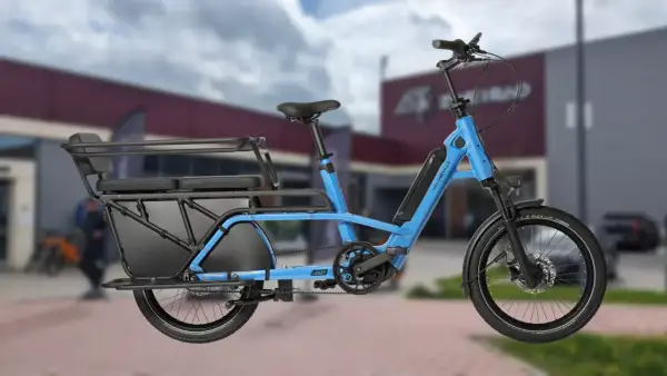 Vélo longtail bleu électrique, idéal pour transporter des passagers ou des courses grâce à sa longue plateforme arrière et ses sièges.