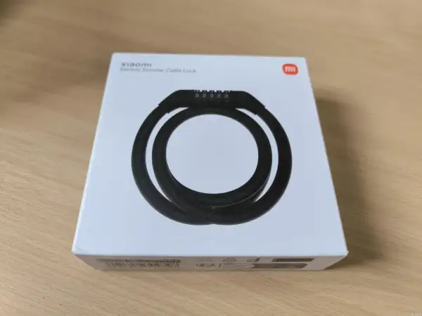 Boîte blanche avec un antivol Xiaomi pour trottinette électrique. Le câble noir est enroulé et un code à 5 chiffres est visible.