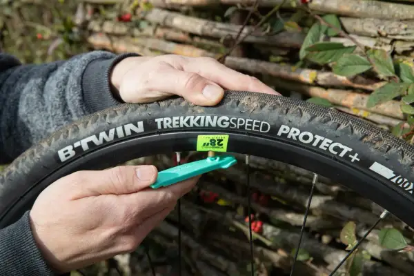 Main d'un cycliste ajustant une chambre à air 700x40c sur une roue de vélo, avec un démonte-pneu vert.