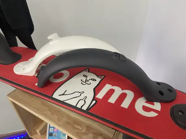 Deux garde boue trottinette Xiaomi, un blanc et un noir, posés sur un deck rouge orné d'un chat.